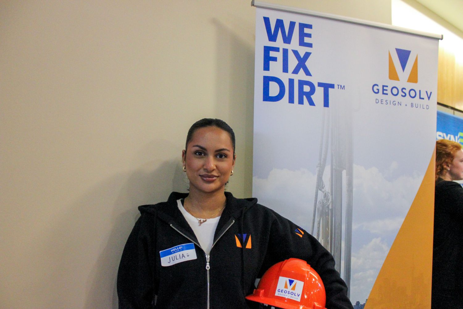 Woman stands in front of a trade booth with a hard hat under her arm