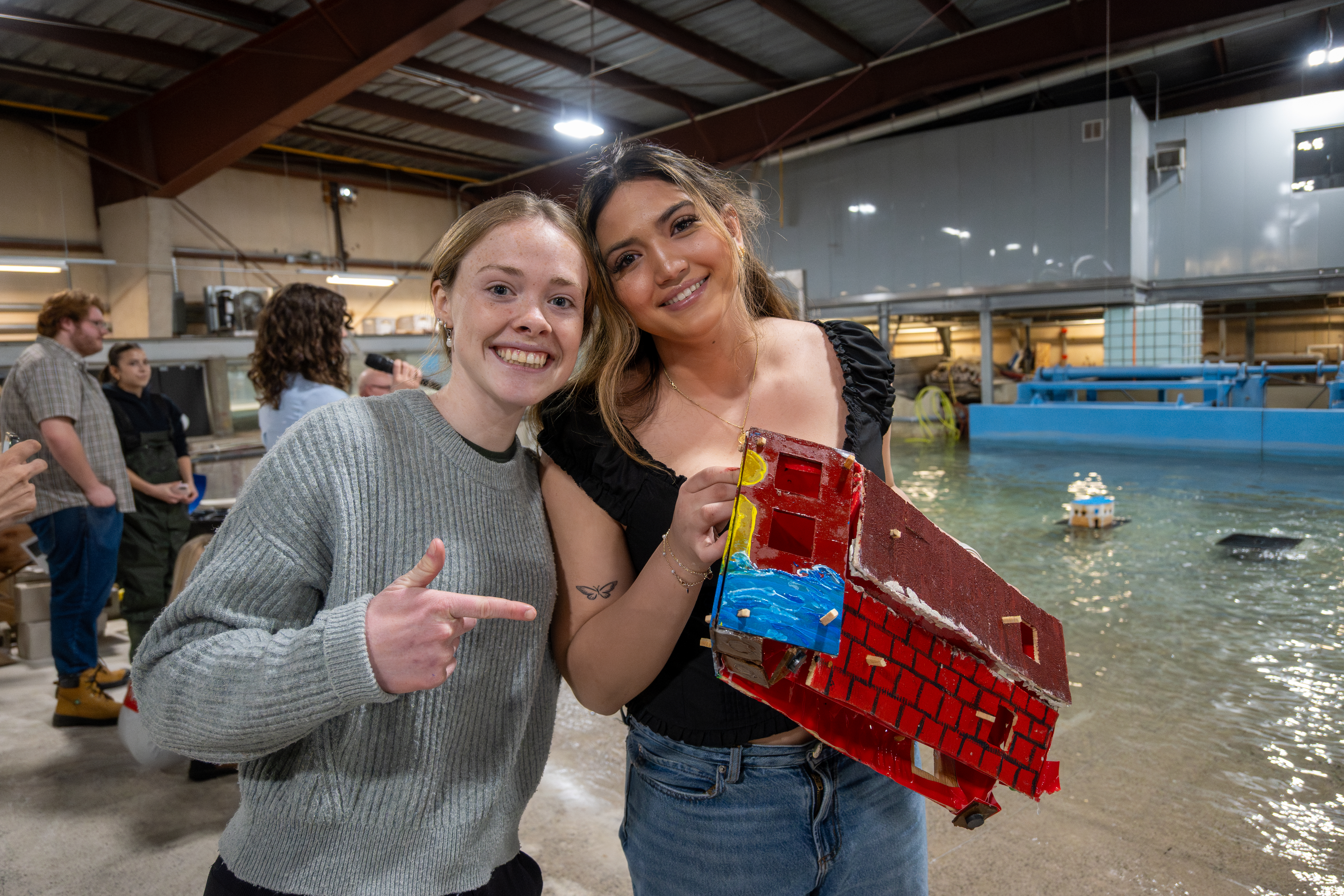 Two young women show off their house model proudly. They are smiling at the camera.