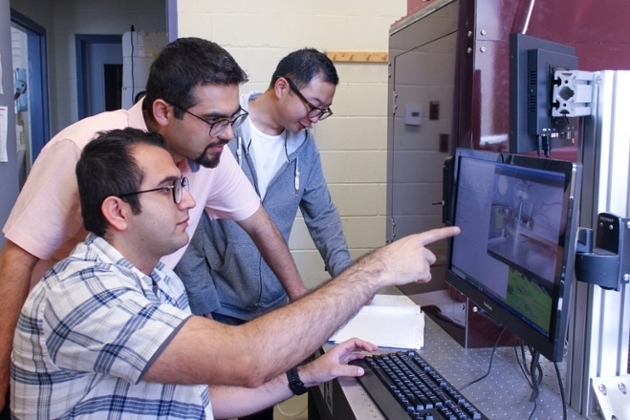 Three researchers in a lab looking at a computer monitor, with one pointing at the screen while another uses the keyboard.