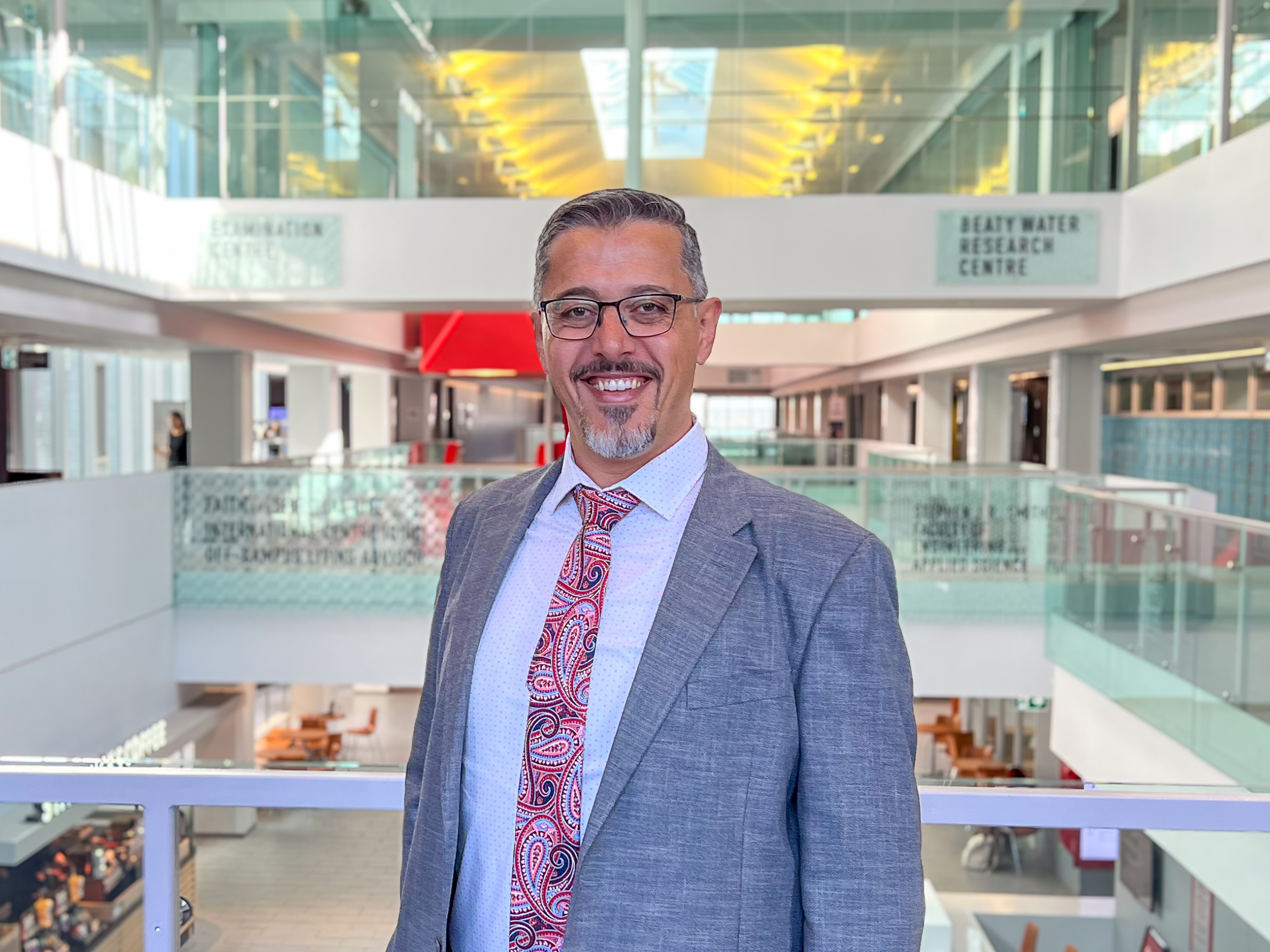 Man with goatee and glasses standing for a headshot in a institutional building