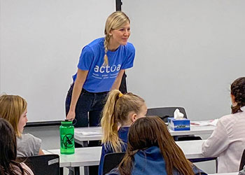 A woman in front of a classroom smiling at a group of children