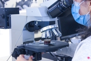 researcher in mask looking into a microscope