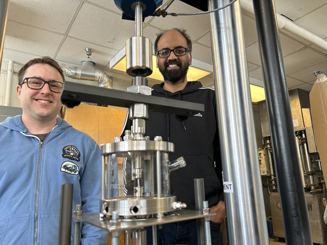 Two men are standing in a lab with a piece of equipment