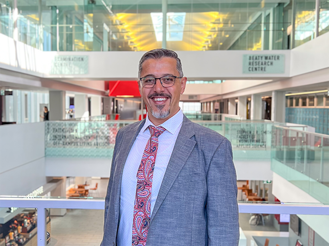Man with goatee and glasses standing for a headshot in a institutional building