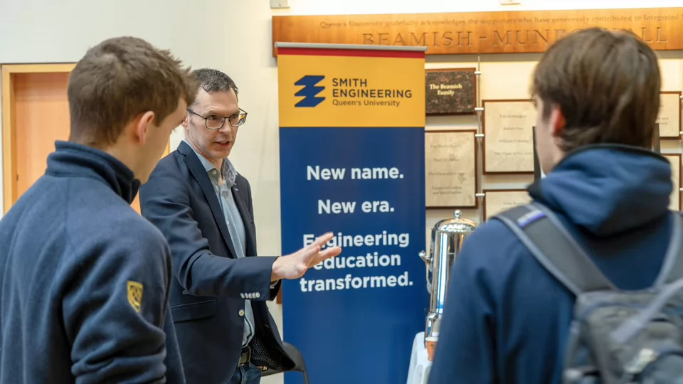 Kevin Mumford speaking with two students beside a Smith Engineering banner.